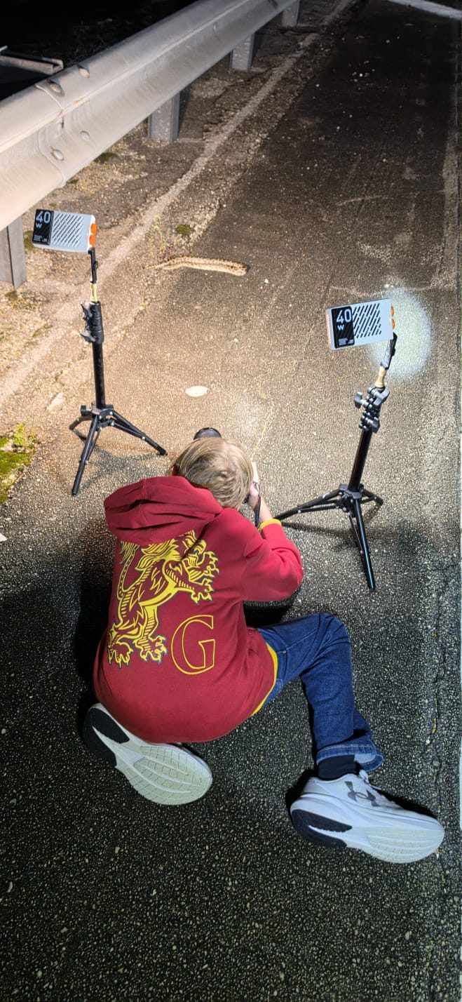 Eduardo crouching on a road at night with a camera and two lights, photographing a snake